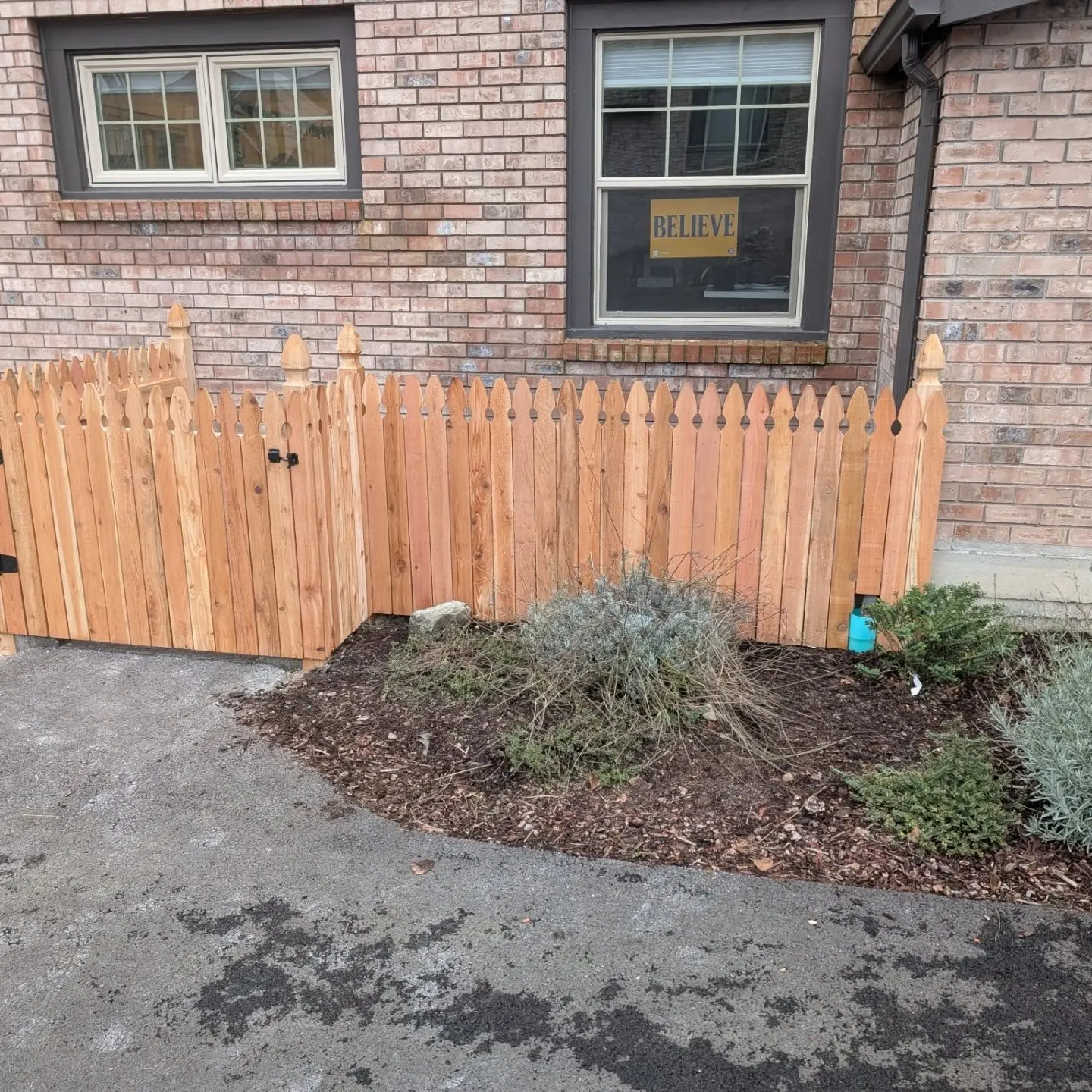 Front view of the new cedar picket fence against a brick wall